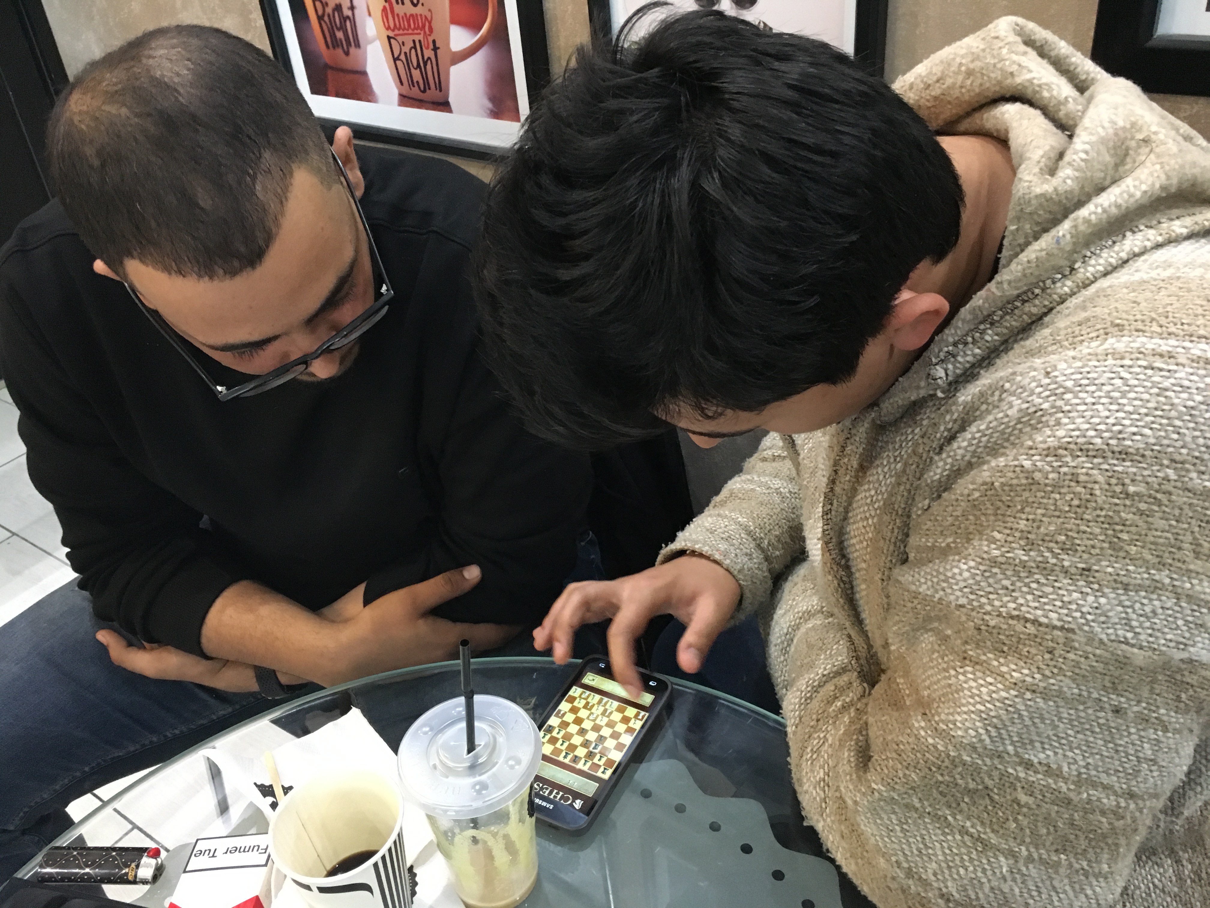 men playing chess on smartphones over coffee