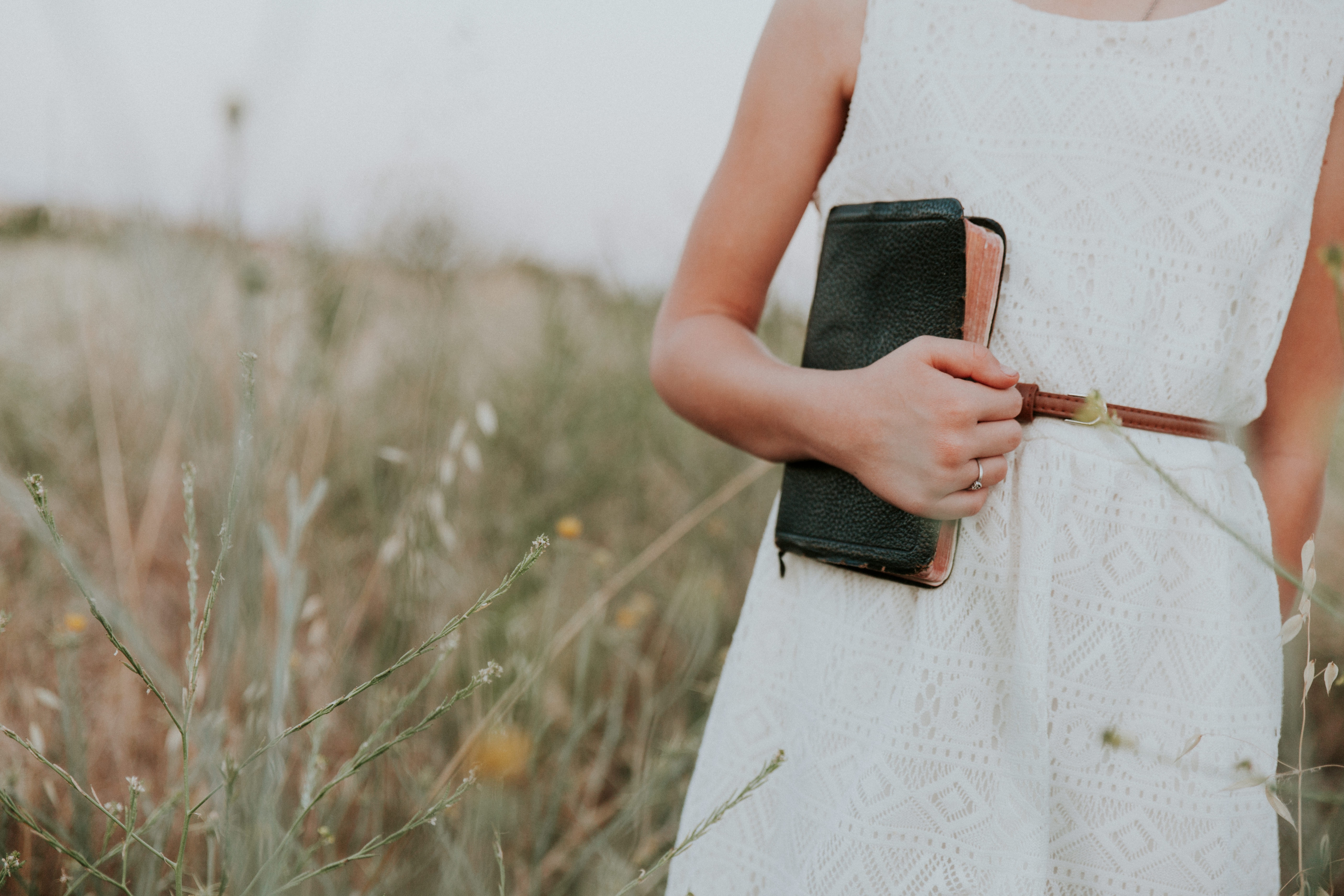 young woman holding bible in field of wild flowers